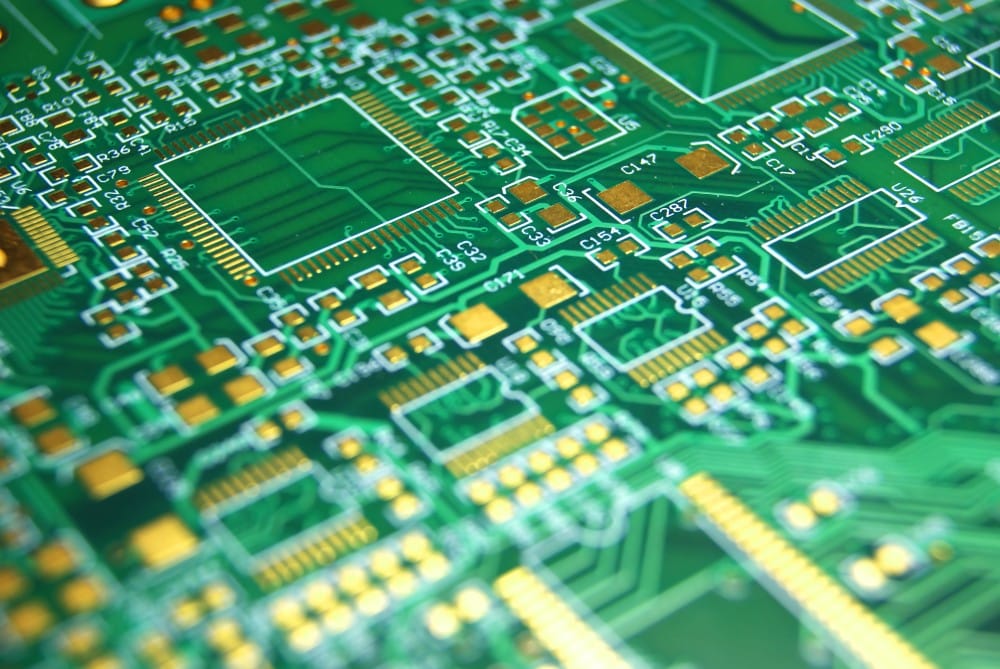 Close-up of a green printed circuit board with gold and white electronic pathways and components.