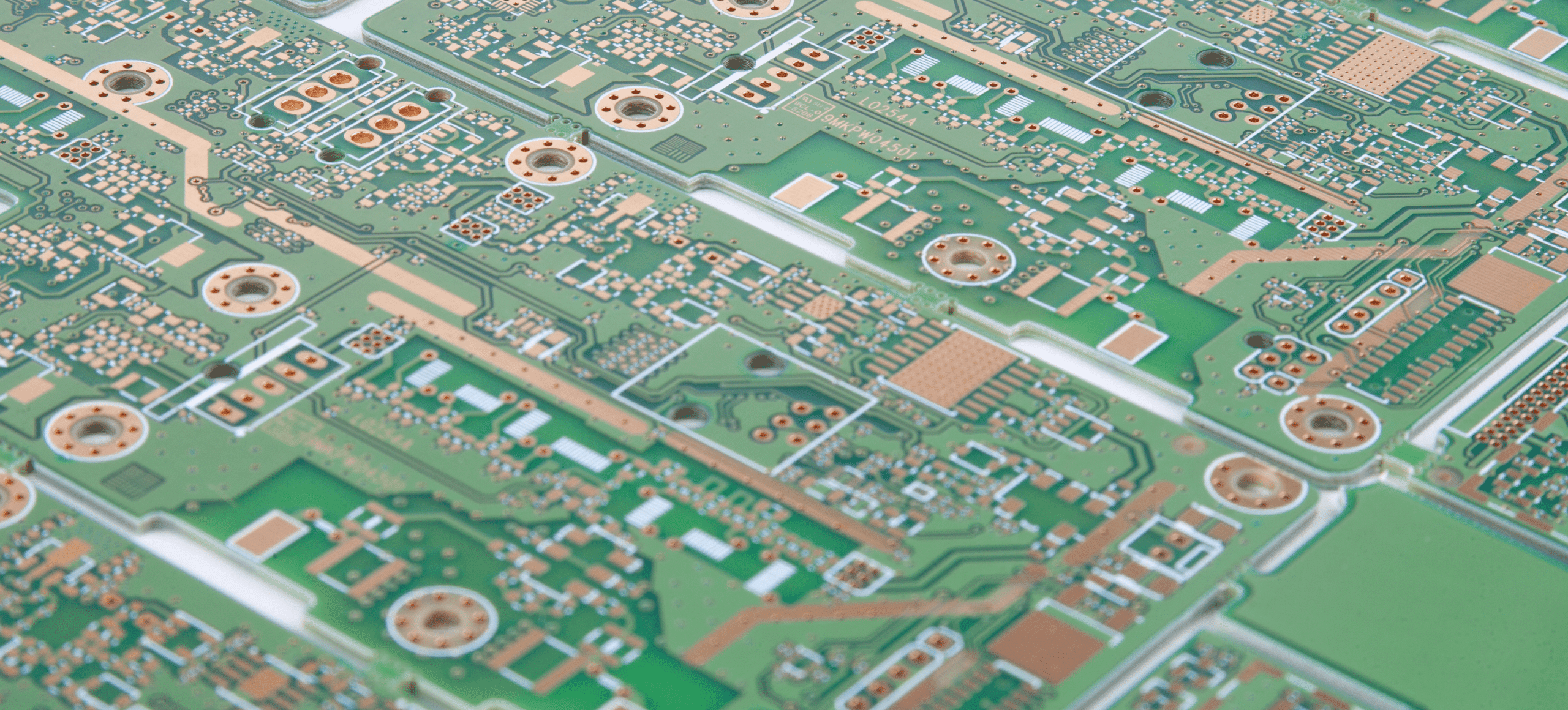 Green circuit board with copper traces and holes, viewed from above at a slight angle.