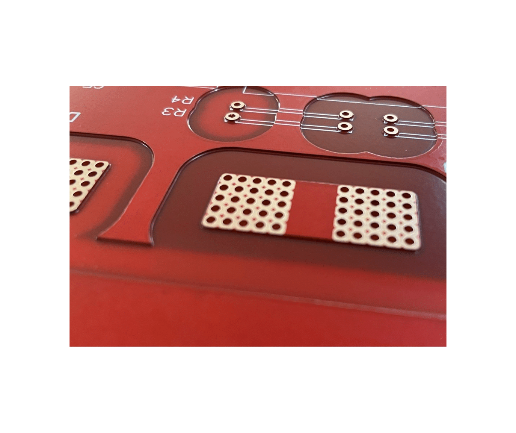 Close-up of a red printed circuit board with multiple holes and copper pads.