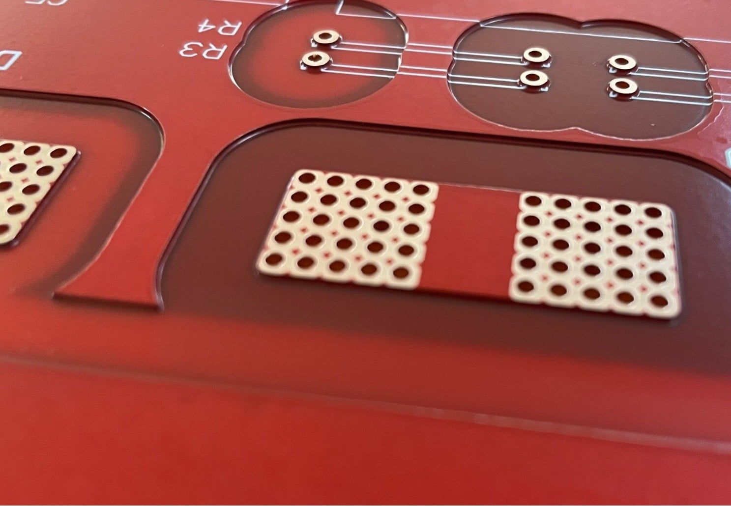 Close-up of a red printed circuit board with multiple holes and copper pads.
