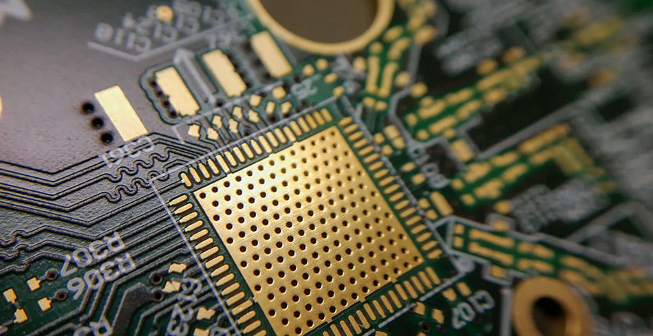 Close-up of a green printed circuit board with gold and copper components and traces.